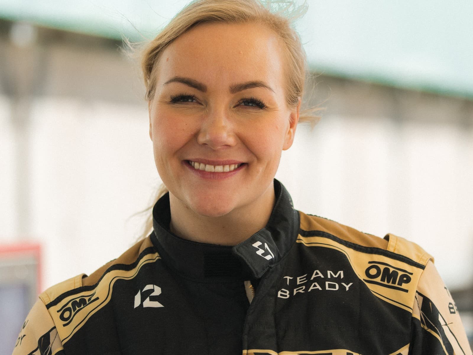 Emma Kimiläinen in Team Brady racing suit at the pit lane, holding racing gear