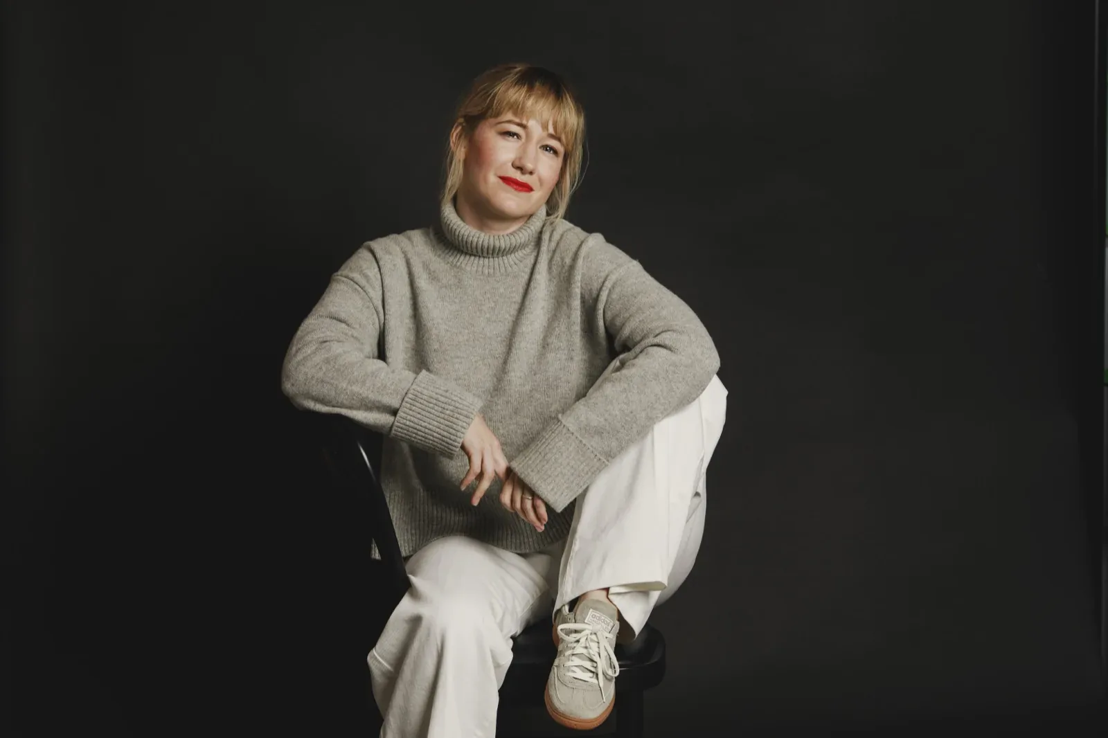 Linda Liukas seated on a black stool in a grey sweater and white trousers