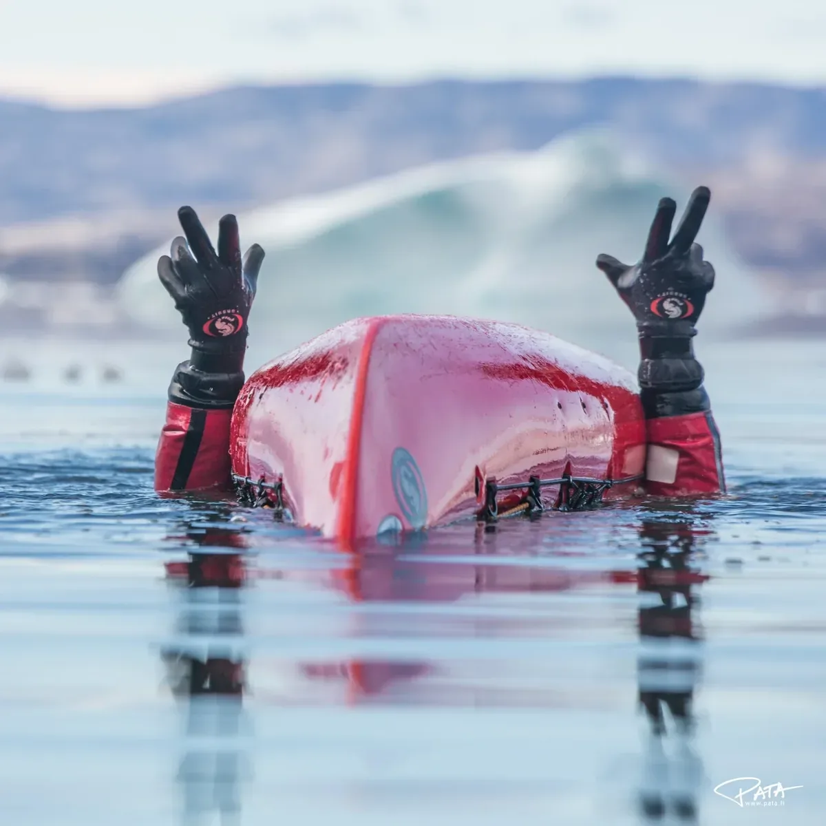 Arms raised from the water beside an overturned red kayak, peace signs with gloves on